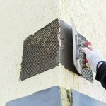 Male builder smear gray wet plaster with a spatula on the facade of the house facade